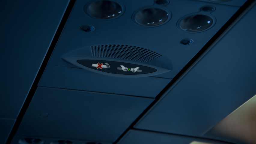 Seat belt notification signal light turns on inside dark lit passenger airplane cabin. Flight safety regulations and procedures in modern aviation rules | Shutterstock HD Video #1063125136