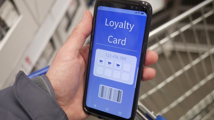 Holding a mobile phone with a loyalty card on the screen at a store to collect rewards and rebates. Royalty-Free Stock Footage #1063128259