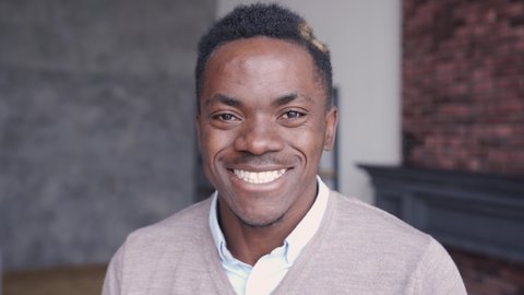 Smiling cheerful young adult african american ethnicity man looking at camera standing at home office background. Happy confident black guy posing for headshot face front close up portrait.