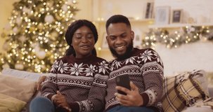 Young african american couple using smartphone, talking to family, congratulaings Merry Christmas by video call conference app. New 2021 Year congrats remotely concept