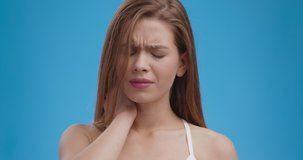 Close up portrait of young upset woman massaging her sore neck, feeling spine ache, muscle pain, blue studio background