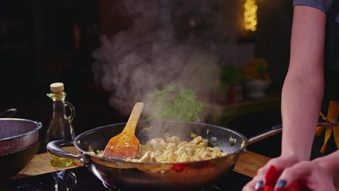 Woman cooking frying meat and vegetables in wok pan on kitchen table. Closeup hands. Real, authentic cooking.