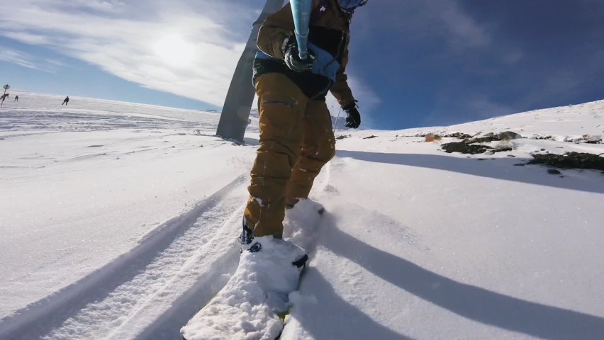 Man on snowboard riding fast on the mountain slope and filming himself with camera. Concept of winter extreme sports, active recreation.