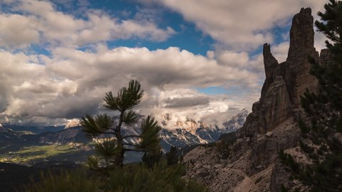 Motion time lapse of thick white clouds moving over rocky mountain peaks of the dolomites in Italy, in the foreground you can see the cliffs of Cinque Torri with forests of pine trees below.