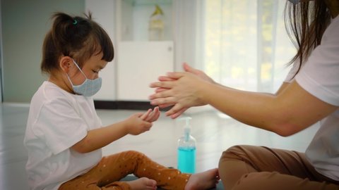  Mother teaching daughter putting on a protective mask on face , using Sanitizer hand gel before going outdoors. Medical mask to prevent coronavirus. Coronavirus pandemic.
