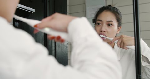 beautiful Asian woman brushes her teeth in front of mirror. pretty young lday Using electric toothbrush in the bathroom