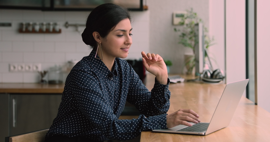 Indian ethnicity attractive business woman sitting at bar counter in modern cozy kitchen texting on portable computer, e-mailing to client, search information, do telecommute job remotely from home | Shutterstock HD Video #1063141672