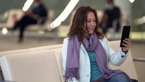 female passenger is resting in lounge area in airport, chatting online by smartphone