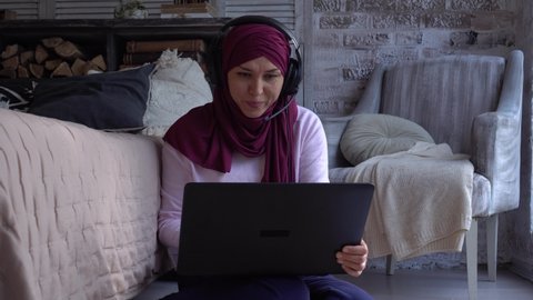 Happy smiling friendly Muslim woman working remotely from home. Online chat, business conference using headphones, microphone and laptop. Remote work, freelance, lockdown. Distance learning teacher