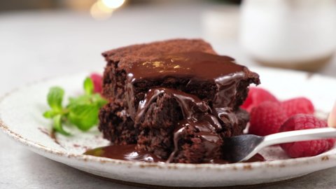 Eating brownie with fork. Taking bite of chocolate cake with chocolate icing and raspberries