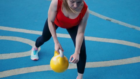 Young female athlete doing workout, training with a kettlebell in the open air. blue background