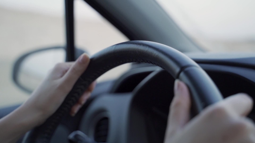 Close up of young woman's hands on vehicle steering wheel as she is driving. Female driving a car in the highway, hands move on the wheel in slow motion. Cars pass by in out of focus background