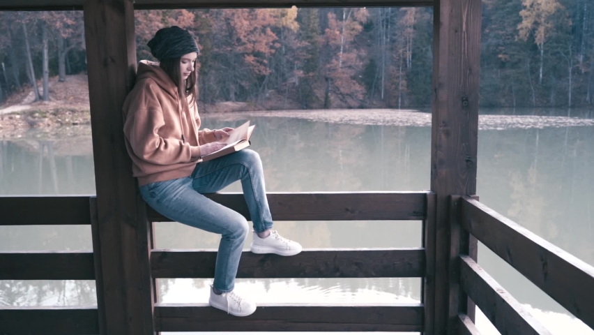 The girl is resting on a hike. Read a book on the shore of a mountain lake. Slow motion video.
