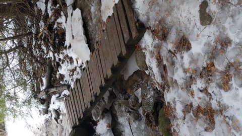 Vertical Video, River Rushing Under Wooden Bridge on Snowy Winter Hiking Path