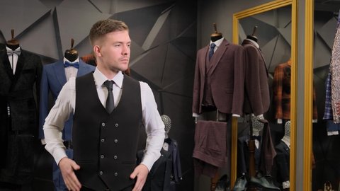 a man trying on a vest. Businessman looks in the mirror on his reflection at the mirror. Businessman looks in the mirror in a men's clothing store.