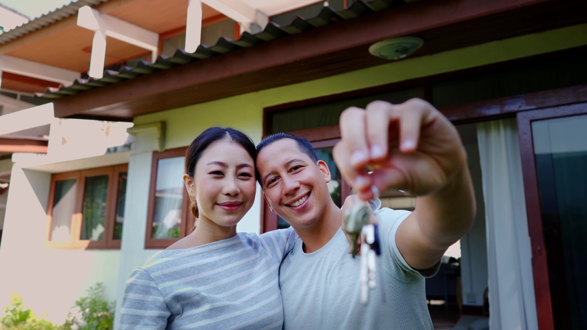 Portrait of 30s young adult Asian couple holding a new property key with excitement. Husband and wife real estate owners in Asia. Housing investment achievement concept - 4K Slow Motion Footage Royalty-Free Stock Footage #1063165624