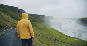 Male tourist wearing yellow raincoat at Gullfoss Waterfall on Iceland in Icelandic nature.