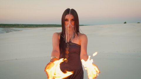 Beautiful young mysterious woman with fire in her hands posing at the camera.