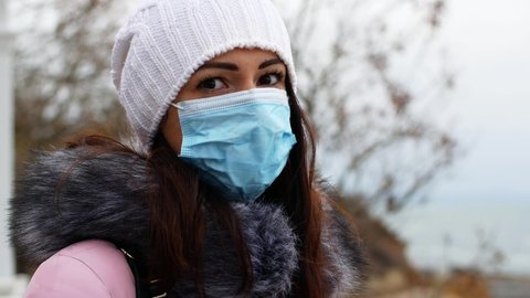 A woman with long dark hair in a mask from air pollution and the Covid19 coronavirus walks in the park. Close-up of a woman in a mask protecting against coronavirus outdoors. Stay at home.
