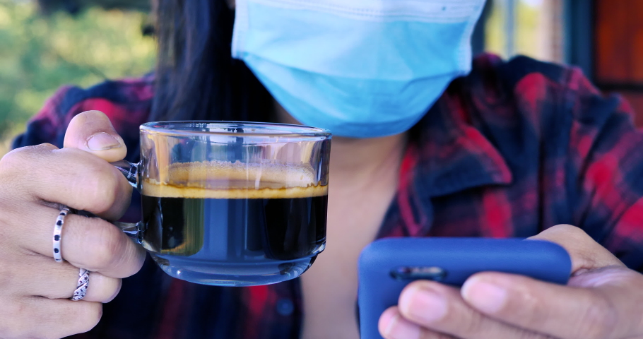 Woman hand holding a cup of black coffee, woman wearing mask in a cafe