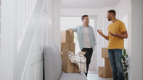 Camera tracks across hallway to show male couple carrying boxes as they move into new home together - shot in slow motion