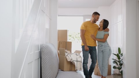 Camera tracks across hallway to show excited couple hugging as they move into new home surrounded by boxes - shot in slow motion