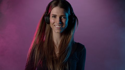 Slow motion of young woman listening music with neon lights background. Filmed on high speed cinema camera.