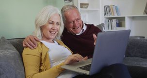 Happy senior caucasian couple making video call using laptop computer, waving and smiling sitting at home sitting on sofa, in slow motion. quality time together at home during coronavirus covid 19