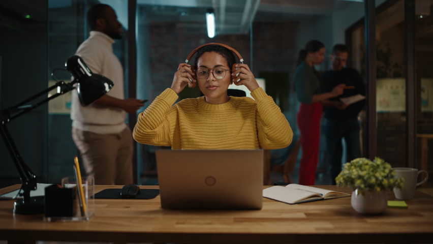 Young Latin Project Manager Putting On Headphones and Working on Laptop Computer in Busy Creative Office Environment. Beautiful Diverse Multiethnic Female Specialist is Writing Business Strategy. | Shutterstock HD Video #1063172956