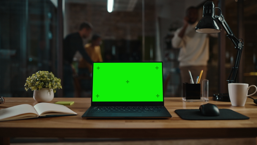 Zoom In Footage of a Laptop Computer with Green Screen Mock Up Display on a Desk in a Busy Creative Office Environment. Isolated Template for Any Media Type. Authentic Hipster Agency Vibe. Royalty-Free Stock Footage #1063172959