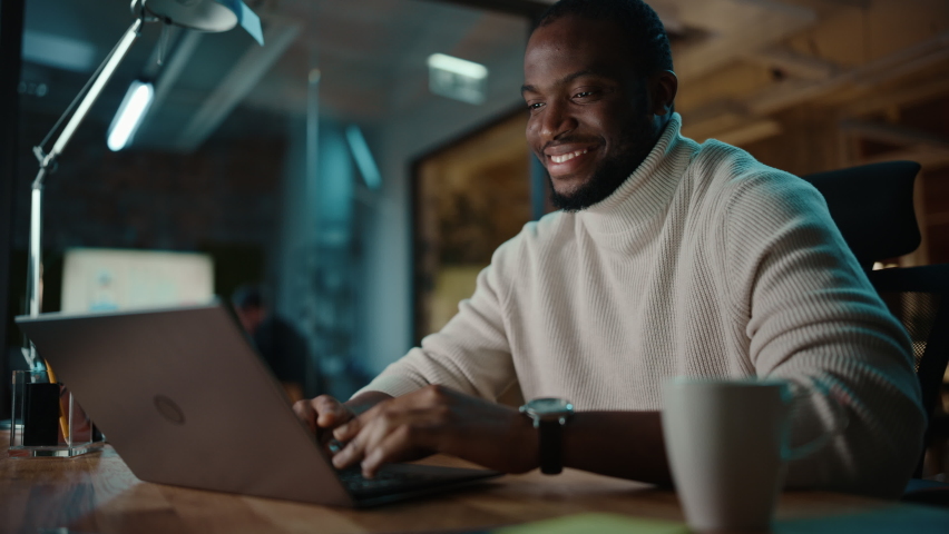 Handsome Black African American Man Having an Online Conversation on a Laptop Computer in Creative Office Environment. Happy Male is Browsing Social Media and Replying to Friends in Messenger. | Shutterstock HD Video #1063172995