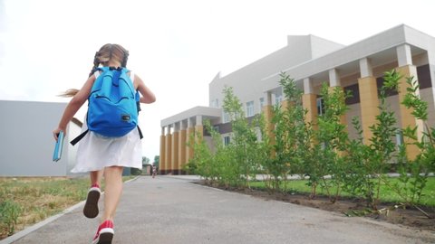 little girl kid with a backpack and a textbook runs hurrying to school. education concept. little schoolgirl with a backpack fun runs to the school building. child running with textbook back view