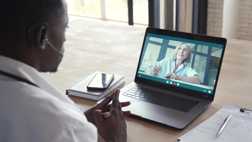 Black male doctor consulting senior old patient by telemedicine online video call. African physician using telehealth medical chat virtual healthcare appointment on laptop computer. Over shoulder view Royalty-Free Stock Footage #1063174120