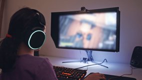 Young girl sitting in front of a computer, playing a game wearing a headset