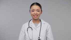 medicine, profession and healthcare concept - video portrait of happy smiling asian female doctor in white coat with stethoscope showing how to use medical mask over grey background