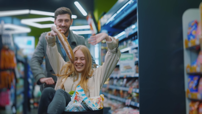Happy young family couple carries a girl in a grocery basket shopping in supermarket. Smiling lovely husband and wife buyers customer grocery store concept. Slow motion Royalty-Free Stock Footage #1063180327