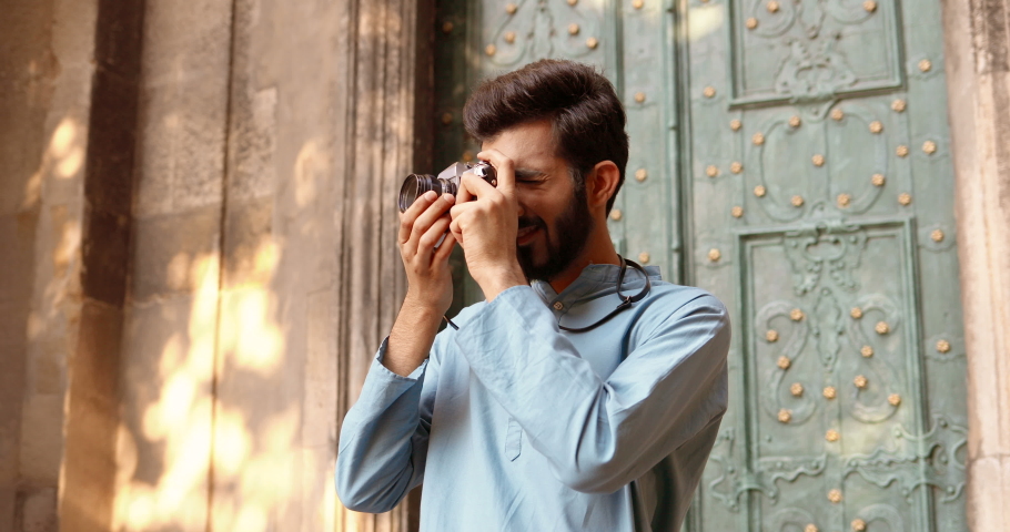 Young Hindu handsome stylish man photographer taking photo at street with photo camera. Antique town. Male tourist making pictures outdoors. Guy from India travelling and working. | Shutterstock HD Video #1063181683