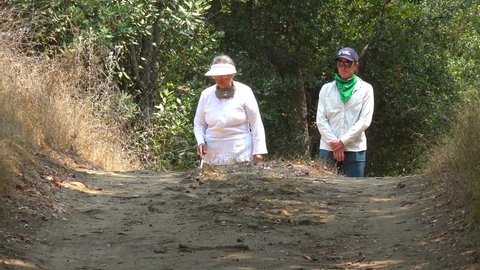 CALIFORNIA - CIRCA 2020 - A blind woman walks with a cane through a natural area with a guide helping her explore the wilderness.