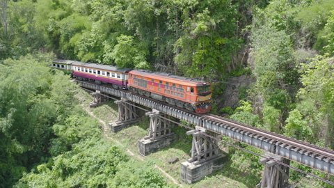 Aerial view of Thai local old classic train on railway on River Kwai Bridge in Kanchanaburi town, Thailand in public transportation concept.