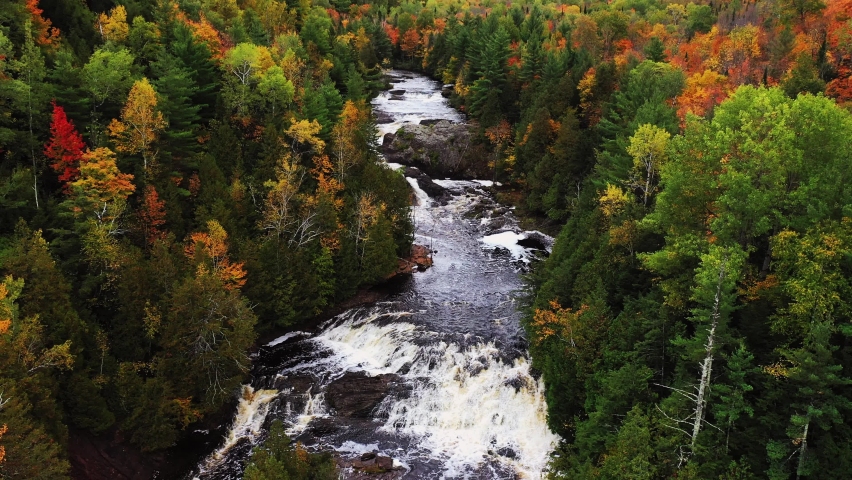 Beautiful panning down aerial looking down the Potato River to Upper Potato River Falls coming down to a close up below the lower falls as heavy water flow cascades over the rocky surface.
