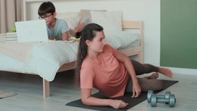 Home Isolation, Distance Learning, Remote Work, Fitness at Home, Online Training, Family Quarantine. Mom goes in for sports at home on the floor next to her son who does homework on the bed