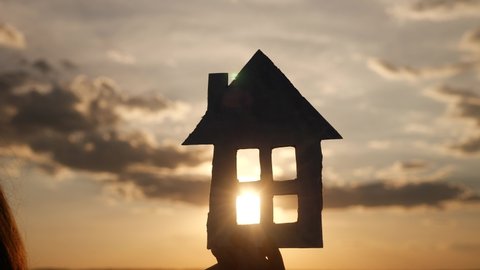 paper house in hand silhouette at sunset. insurance mortgage home market concept. handmade paper house in the sun lifestyle at sunset silhouette. dream of home accumulation symbol
