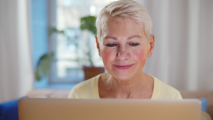 Excited older woman looking at laptop screen rejoicing winning lottery. Portrait of aged happy lady clapping hands and enjoying good news on computer Royalty-Free Stock Footage #1063189999