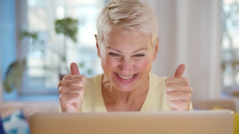 Excited older woman looking at laptop screen rejoicing winning lottery. Portrait of aged happy lady clapping hands and enjoying good news on computer