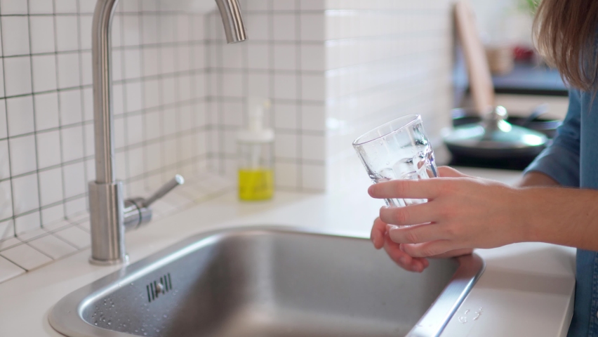 Woman pouring clean filtered water from the tap in glass for drinking at modern loft style kitchen   | Shutterstock HD Video #1063190245
