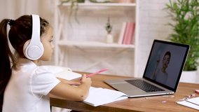 little child girl using laptop for doing school tasks at home and writing notes. online lesson at home