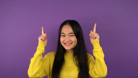 happy smiling young asian woman on isolated purple background shows up index finger. Free space for object or text 4K
