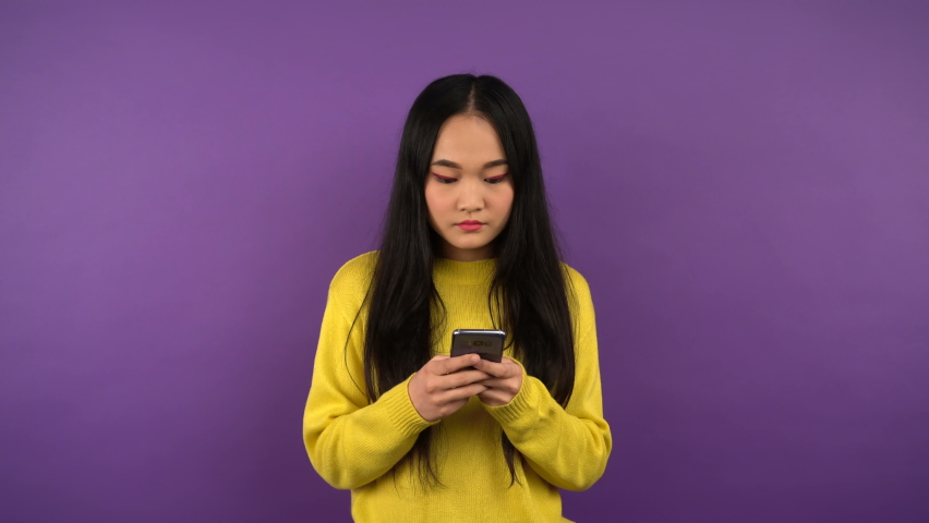 a woman with a smartphone in her hands looks to the right and left while making a choice. isolated purple background. 4K Royalty-Free Stock Footage #1063191691