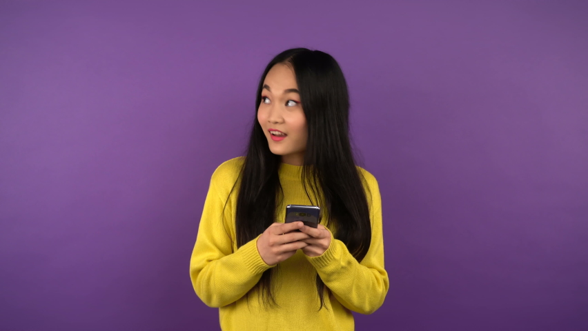 a woman with a smartphone in her hands looks to the right and left while making a choice. isolated purple background. 4K Royalty-Free Stock Footage #1063191691