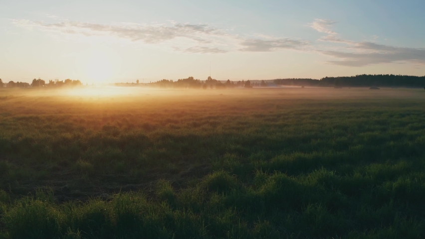 Arial view of a field during summer in sweden. Sun rays beaming thrugh fog during golden hour. Royalty-Free Stock Footage #1063192480